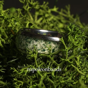 May include: A silver ring with a band of green and white speckled stone. The ring is set against a backdrop of vibrant green moss. The text "napoleonbands" is visible at the bottom of the image.