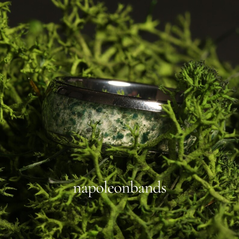 May include: A silver ring with a band of green and white speckled stone. The ring is set against a backdrop of vibrant green moss. The text "napoleonbands" is visible at the bottom of the image.