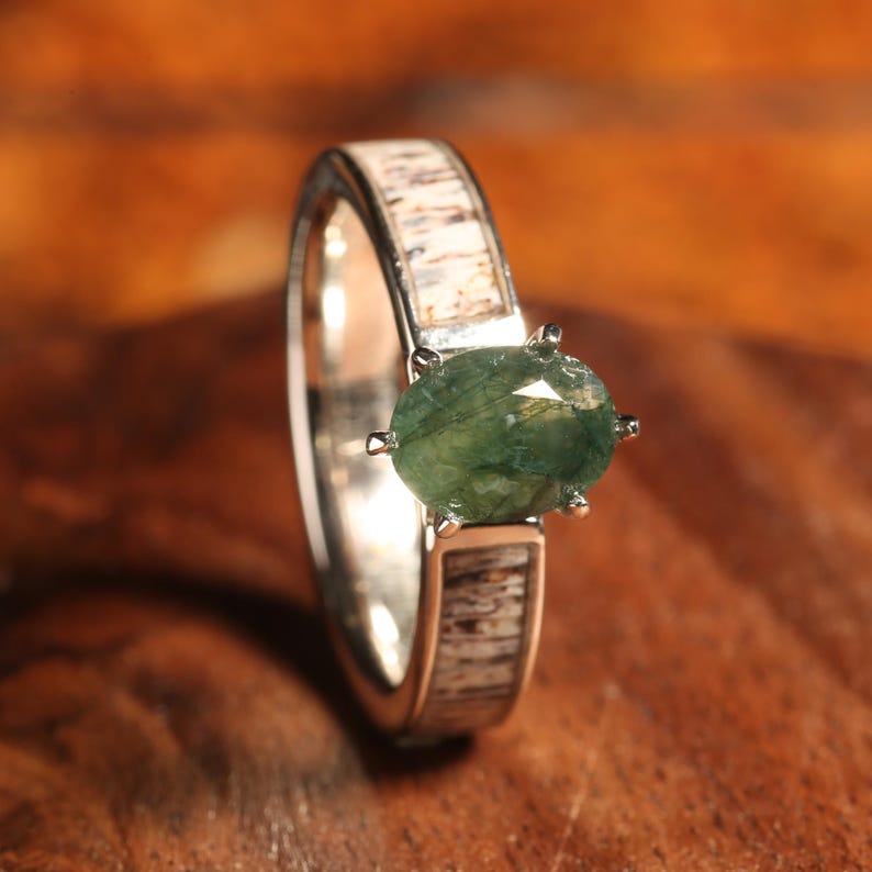 May include: A silver ring with a green gemstone set in a prong setting. The band of the ring is made of antler.