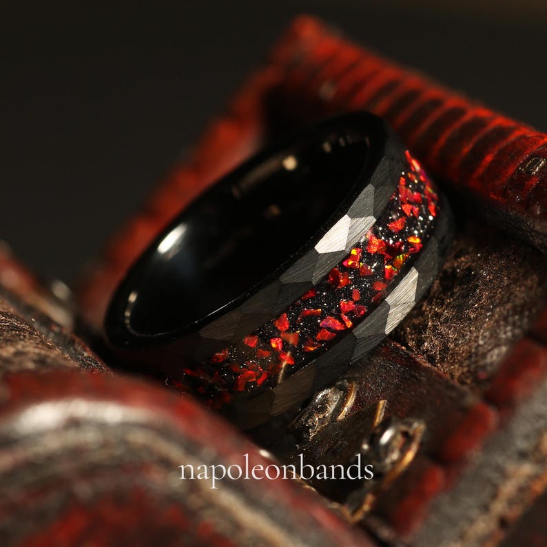 May include: A black tungsten carbide ring with a red and black inlay. The ring has a hammered finish and is set in a wooden box.