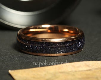 May include: A rose gold band with a dark blue inlay of sparkly blue sand. The band is a simple design with a smooth finish.