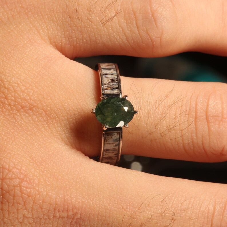 May include: A ring with a green gemstone set in a silver band. The band is made of antler and has a natural wood grain pattern.