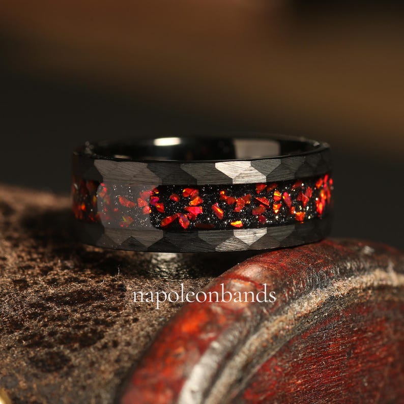 May include: Black tungsten carbide ring with a red and black inlay. The ring has a textured, hexagonal pattern.