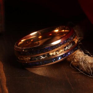 Puede incluir: Un anillo de oro rosa con una incrustaci&oacute;n azul y negra y motas doradas. El anillo est&aacute; hecho de metal y tiene un acabado pulido.
