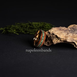 May include: A gold-colored ring with a wood and green stone inlay. The ring features a polished finish and is set against a dark background with the text "napoleonbands". The ring's design incorporates natural elements.