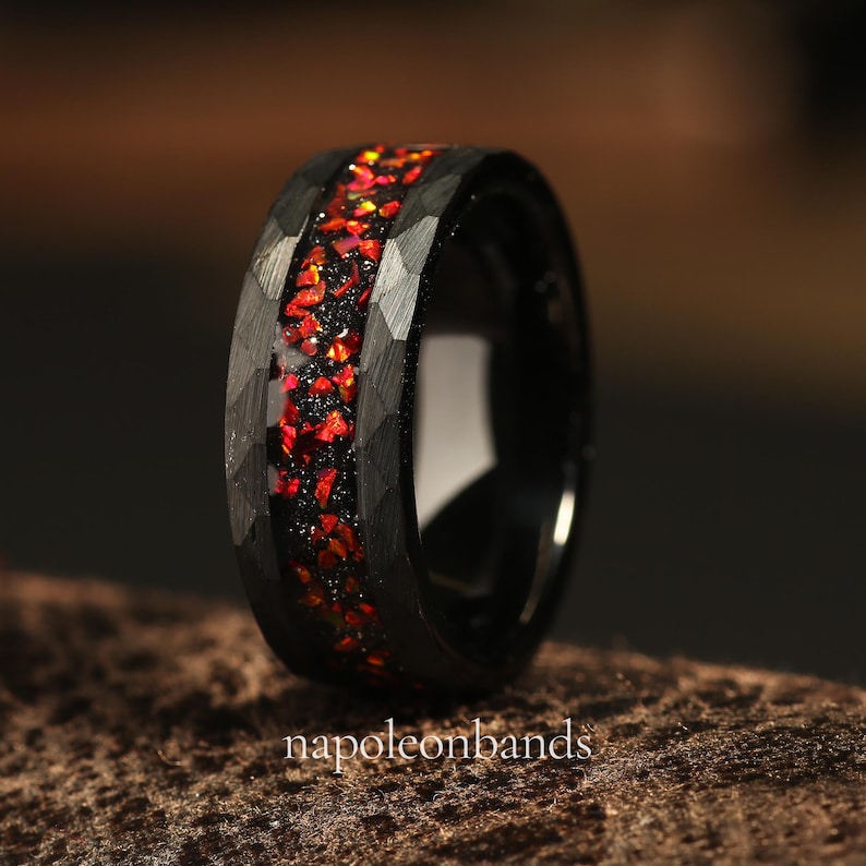 May include: A black tungsten carbide ring with a red and orange glitter inlay. The ring has a hammered finish.
