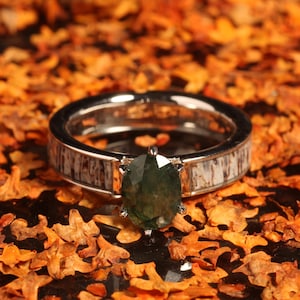 May include: A silver ring with a green gemstone set in a white and brown deer antler band.