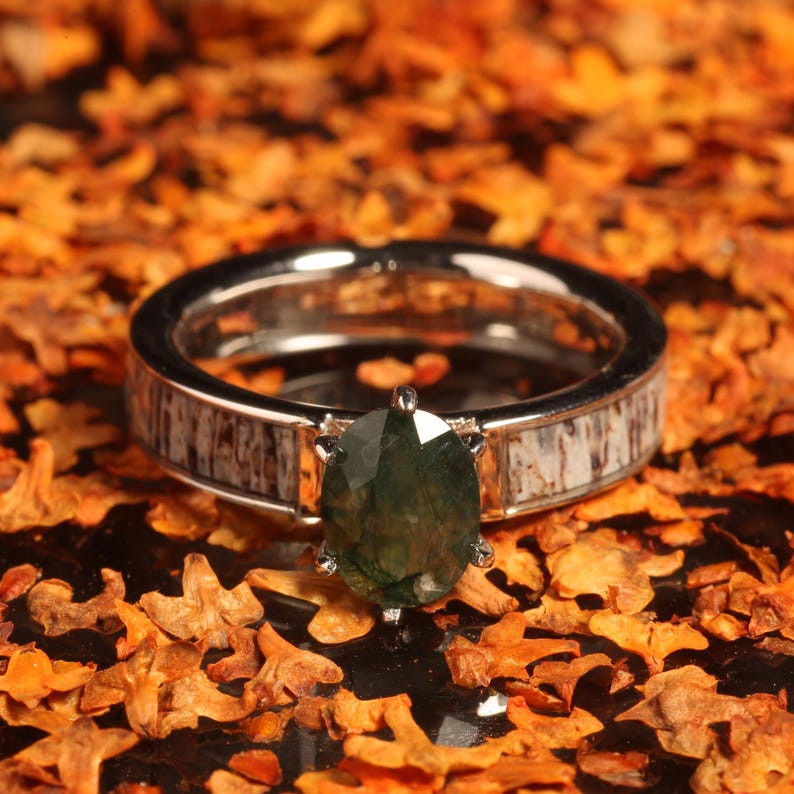 May include: A silver ring with a green gemstone set in a white and brown deer antler band.