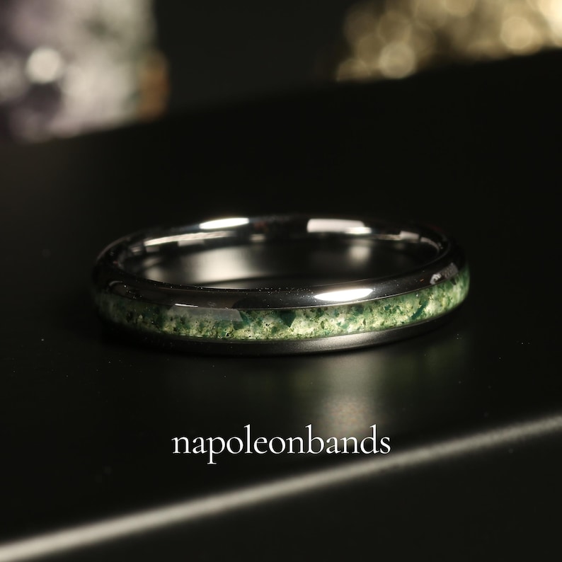 Pode incluir: Um anel de prata com uma incrusta&ccedil;&atilde;o de pedra verde. O anel est&aacute; sobre uma superf&iacute;cie preta. O texto "napoleonbands" &eacute; vis&iacute;vel na parte inferior central da imagem.