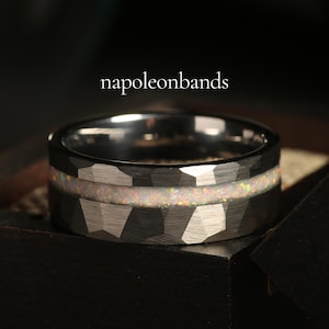 May include: A silver tungsten carbide ring with a hammered finish and a thin band of iridescent opal inlay. The ring is in a black box.