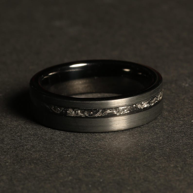 May include: A black tungsten carbide ring with a brushed finish and a silver-colored engraved band.