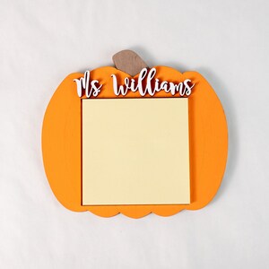 May include: Orange pumpkin-shaped wooden sign with a white sticky note and the text "Mrs. Williams" in white letters.