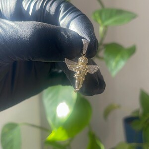 May include: A gold cherub pendant with diamond accents. The pendant is in the shape of a cherub with wings outstretched.