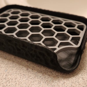 May include: A black soap dish with a gray honeycomb design. The dish has a textured exterior and a raised rim.