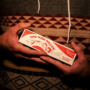 May include: A rectangular white box with red graphics and text that reads ONE WISH WILLOW, CRACK, AMAZE YOUR FRIENDS, and You only get ONE WISH. The box features illustrations of two faces and small stars, presented in a horizontal orientation.