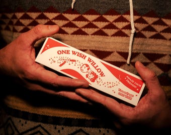 May include: A rectangular white box with red graphics and text that reads ONE WISH WILLOW, CRACK, AMAZE YOUR FRIENDS, and You only get ONE WISH. The box features illustrations of two faces and small stars, presented in a horizontal orientation.