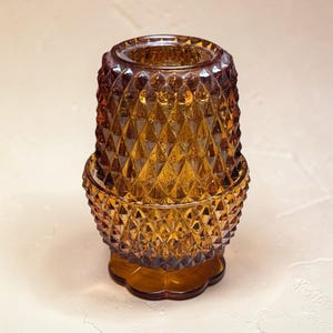 Puede incluir: Candelabro de vidrio color ámbar con un patrón de diamantes. El candelabro tiene una base redonda y una parte superior acampanada. El vidrio tiene un brillo cálido, perfecto para agregar ambiente a cualquier habitación. Es un artículo decorativo.