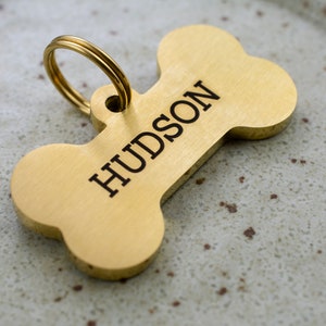 May include: A gold bone-shaped dog tag with the name "HUDSON" engraved on it.