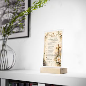 Peut inclure: Une plaque rectangulaire en acrylique présentant le texte du Psaume 91, ornée d'illustrations florales et d'une croix, fixée sur un socle en bois clair. Le design inclut des accents dorés, des fleurs blanches et de la verdure sur fond crème.