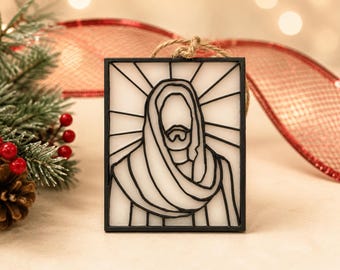 May include: A rectangular ornament featuring a black line art illustration of a figure with a beard and draped head covering against a white background. The design includes radiating lines behind the head and a jute twine loop for hanging.