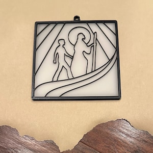 Puede incluir: Arte mural cuadrado negro con un dise&ntilde;o minimalista de dos figuras en una barca, con una figura con halo sosteniendo un bast&oacute;n. El fondo es blanco con l&iacute;neas negras, y el marco tiene un peque&ntilde;o lazo para colgar.