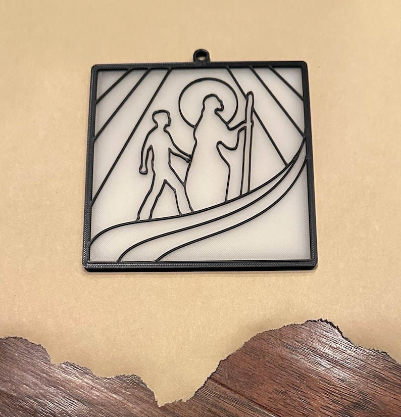 Puede incluir: Arte mural cuadrado negro con un dise&ntilde;o minimalista de dos figuras en una barca, con una figura con halo sosteniendo un bast&oacute;n. El fondo es blanco con l&iacute;neas negras, y el marco tiene un peque&ntilde;o lazo para colgar.