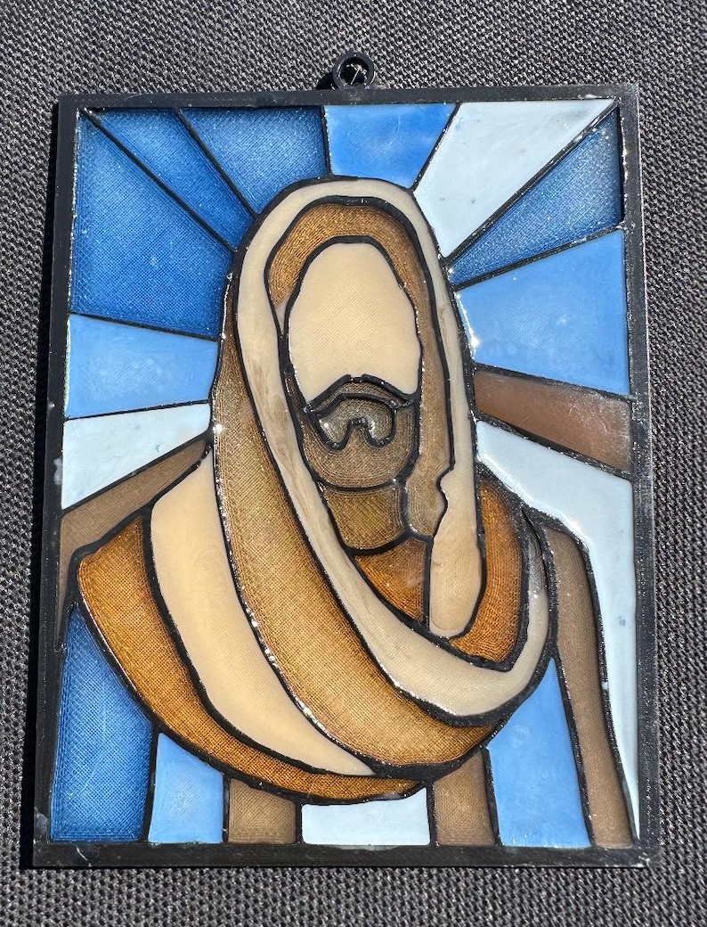 Puede incluir: Panel de vidriera que representa una figura religiosa con barba y t&uacute;nica. La obra de arte presenta una paleta de colores azul, marr&oacute;n y beige, con un borde negro. El dise&ntilde;o recuerda a las vidrieras de las iglesias.