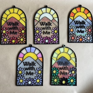 Puede incluir: Cinco colgantes de pared arqueados, estilo vidriera. Cada uno presenta una escena de monta&ntilde;a con un sol, flores y el texto "Walk with Me". Las paletas de colores incluyen tonos de amarillo, naranja, rosa, morado y verde, con bordes negros.