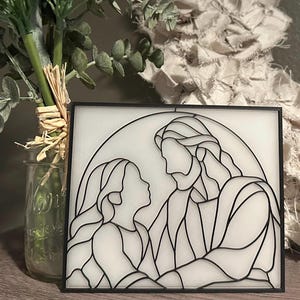 May include: Black and white stained glass artwork depicting a man and a woman looking at each other. The artwork is framed in a black frame.