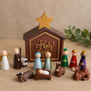 Op de afbeelding: Een houten kerststalset met peg doll figuren van een engel, herder, Maria, Jozef en drie wijzen. Inclusief een bruine stal met een gouden ster en de tekst O Holy Night, plus dierenfiguren van een schaap, koe, ezel en een kameel.