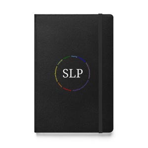 May include: Black notebook with an elastic band closure. The cover features the letters "SLP" in white, surrounded by a circular design with words like "Language" and "Hearing" in various colors. The notebook is closed.