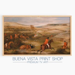 May include: A vintage oil painting depicting a fox hunt in a rural landscape. Riders in red coats are on horseback, pursuing a pack of hounds through a field. The painting is framed in a light wood frame.
