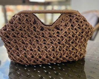 Könnte beinhalten: Eine braune Handtasche mit einem durchbrochenen Häkelmuster und einem strukturierten, integrierten Griff. Die Tasche hat eine breite, V-förmige Öffnung und ein dunkelbraunes Innenfutter, das durch das komplexe, gewebte Fasermuster sichtbar ist.