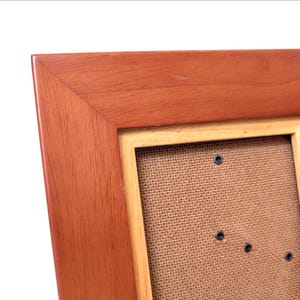 May include: A wooden picture frame with a reddish-brown finish. The frame has a light-colored inner border and a textured backing. The corners are joined at a 90-degree angle. The frame is designed to hold a photograph or artwork.