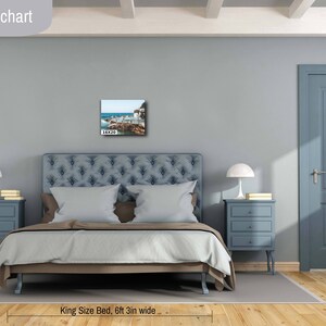 May include: A bedroom interior design mockup with a king-size bed, two nightstands, and a framed photograph of a beach scene above the headboard. The bedroom is painted in a light blue color and has a wooden floor. The bed is made with a light blue duvet and white pillows. The nightstands are made of wood and have three drawers each. The photograph is framed in a black frame. The text "Bedroom size chart" is at the top of the image. The text "16X20 IN / 41X51 CM" is at the bottom left of the image. The text "King Size Bed, 6ft 3in wide" is at the bottom center of the image.