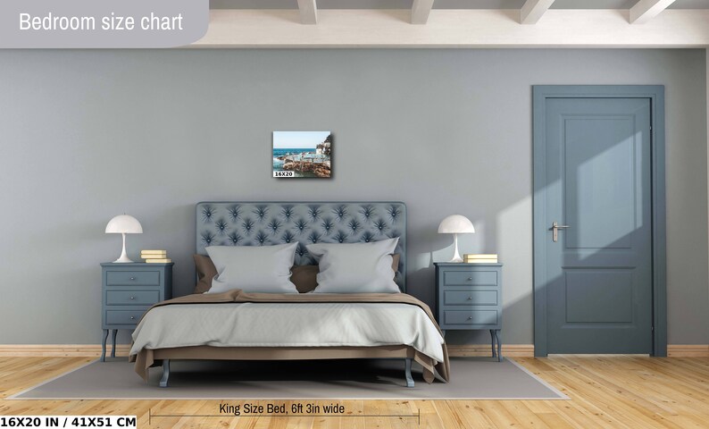 May include: A bedroom interior design mockup with a king-size bed, two nightstands, and a framed photograph of a beach scene above the headboard. The bedroom is painted in a light blue color and has a wooden floor. The bed is made with a light blue duvet and white pillows. The nightstands are made of wood and have three drawers each. The photograph is framed in a black frame. The text "Bedroom size chart" is at the top of the image. The text "16X20 IN / 41X51 CM" is at the bottom left of the image. The text "King Size Bed, 6ft 3in wide" is at the bottom center of the image.