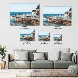 May include: A collage of five different sized photos showing an aerial view of an outdoor pool with people swimming and sunbathing on a rocky island. The photos are arranged in a grid pattern with the largest photo at the top left and the smallest photo at the bottom right. The photos are all in a similar style with a bright blue sky and clear water.