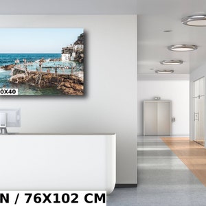 May include: A photograph of a crowded outdoor pool with people swimming and sunbathing. The pool is surrounded by rocks and a blue sky. The image is 30x40 inches.
