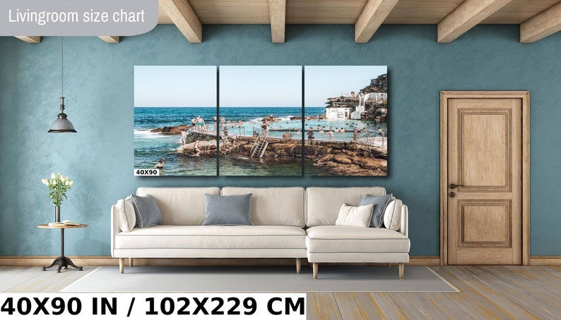 May include: A three-panel canvas print of a beach scene with a pool and people swimming. The print is 40x90 inches and is hanging on a wall in a living room. The text "Livingroom size chart" is at the top of the image.