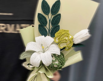 May include: A crocheted bouquet of white lilies, yellow carnations, and green leaves wrapped in light green paper.