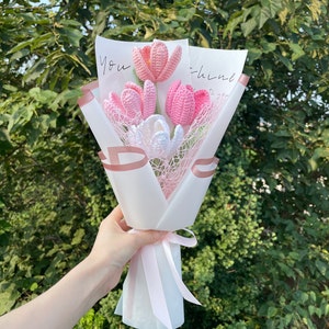May include: A bouquet of pink and white crocheted tulips wrapped in white tissue paper with a pink ribbon. The bouquet has a card that says "You think" on it.