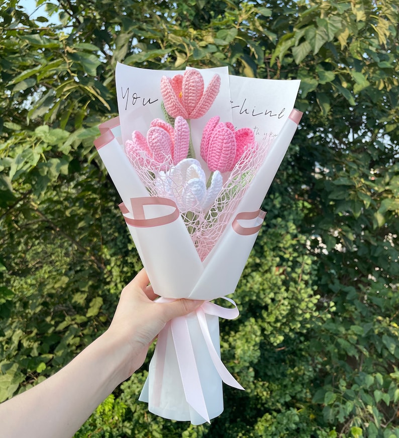 May include: A bouquet of pink and white crocheted tulips wrapped in white tissue paper with a pink ribbon. The bouquet has a card that says "You think" on it.