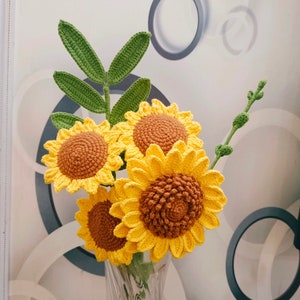 May include: A bouquet of crocheted sunflowers in a clear glass vase. The sunflowers are yellow with brown centers and green leaves.