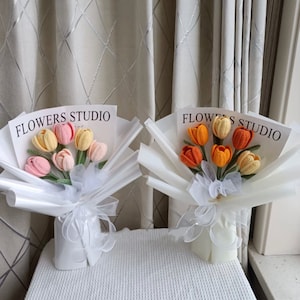 K&ouml;nnte beinhalten: Zwei Str&auml;u&szlig;e geh&auml;kelter Tulpen in wei&szlig;em Verpackungspapier. Die Str&auml;u&szlig;e sind mit "Flowers Studio" beschriftet. Ein Strau&szlig; hat rosa, orange und gelbe Tulpen. Der andere Strau&szlig; hat orange und gelbe Tulpen.