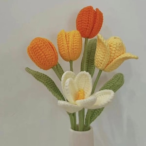 May include: A bouquet of crocheted flowers in a white vase. The flowers are orange, yellow, and white. The flowers are arranged in a vase with a white background.
