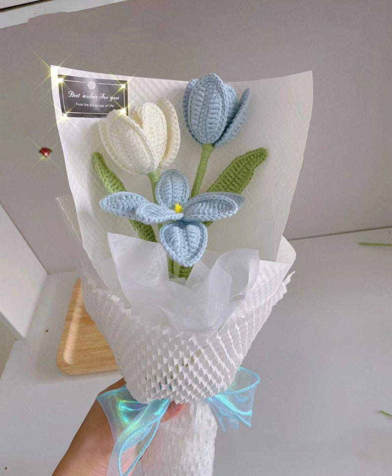 May include: A bouquet of crocheted flowers in blue and white, wrapped in white tissue paper and tied with a blue ribbon. The card attached to the bouquet reads "Best wishes for you, from the blessings of life."