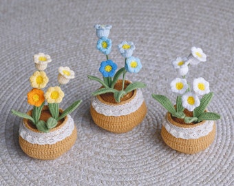 Puede incluir: Tres arreglos florales de ganchillo en pequeñas macetas marrones con ribete de encaje blanco. Las flores son amarillas y naranjas, azules y blancas.