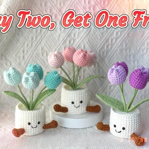 May include: Three crochet tulip plants in white pots with smiling faces and brown feet. The tulips are in shades of blue, pink, and purple. The text "Buy Two, Get One Free" is at the top of the image.