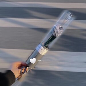 K&ouml;nnte beinhalten: Eine einzelne, silberne, perlenbesetzte Blume in einer transparenten Plastikh&uuml;lle, verpackt in grauem Papier mit einem wei&szlig;en Herzaufkleber. Der Stiel ist gr&uuml;n. Ein Band mit Text ist um die Basis gebunden.
