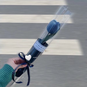 K&ouml;nnte beinhalten: Eine blaue geh&auml;kelte Tulpe in einer transparenten Plastikr&ouml;hre, gebunden mit einem marineblauen Band. Die Blume ist in einer transparenten R&ouml;hre mit marineblauem Boden verpackt. Der Text auf dem Etikett lautet "Mini wishes like heaven in general which is sweet".